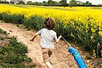 Rear view of boy running along yellow flower field track pulling fish kite