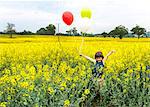 Boy standing in yellow flower field holding red, yellow and white balloons