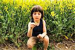 Boy crouching looking at yellow flower from field