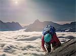 Climber on a rocky wall above a sea of fog in an alpine valley, Alps, Canton Wallis, Switzerland