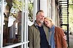 Mature couple leaning against window smiling