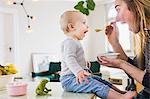 Baby girl mimicking mother whilst eating  at kitchen table