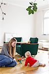 Mid adult woman and baby daughter play with building blocks on living room floor