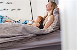 Tired woman and baby daughter lying bed with coffee