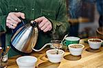 Man pouring boiling water into coffee bowls for tasting on coffee shop counter