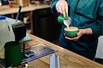 Cropped shot of male barista pouring milk into coffee cup in coffee shop