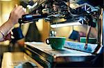 Hands of male barista heating milk jug on coffee machine in coffee shop