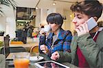 Two sisters in cafe using laptop, digital tablet and smartphone