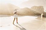 Rear view of woman strolling with parasol on sunlit beach, Cape Town, South Africa