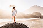 Woman standing on rock with parasol on sunlit beach, Cape Town, South Africa