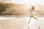 Woman jumping mid air with parasol on sunlit beach, Cape Town, South Africa