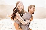 Woman getting piggy back from boyfriend on sunlit beach, Cape Town, South Africa