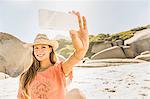 Woman wearing straw hat taking smartphone sellfie on beach, Cape Town, South Africa