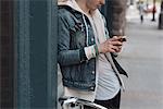 Young man leaning against wall, using smartphone, mid section