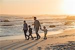 Happy young family walking on the beach at sunset