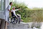 Female nurse assisting senior man in wheelchair on porch