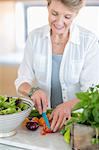 Happy senior woman cutting vegetables in kitchen