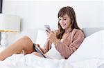 Happy woman reclining on the bed using a mobile phone