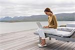 Happy beautiful woman using a laptop at lakeshore