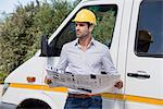 Male engineer reading a blueprint by van at site