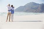 Rear view of a couple standing with arm around each other on the beach