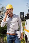 Male engineer talking on a mobile phone by van at site