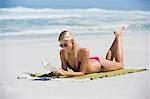 Young woman lying on the beach reading a book