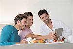 Happy male friends taking selfie with tablet on breakfast table at home