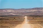 A 4x4 car leaves a cloud of dust as it apporachs along the long dusty road to the Fish River Canyon, Namibia, Africa