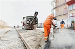 Rear view of manual worker laying asphalt at construction site