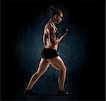 Muscular woman with dumbbell on dark background