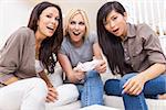 Three beautiful interracial young women friends at home having fun playing video console games together and laughing