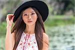 Outdoor portrait of a beautiful thoughtful young Chinese Asian young woman or girl wearing a summer dress and a black hat
