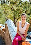 Get inspired by Park Guell in your next trip to Barcelona, Spain. Portrait of happy young woman sitting on trencadis style fence