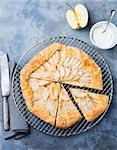 Apple galette, pie, tart with cinnamon on cooling rack on a blue stone background. Top view