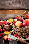 Fresh ripe summer berries and fruits (peaches, apricots, cherry and strawberry) in wicker basket