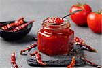 Tomato and chili sauce, jam, confiture in a glass jar on a grey stone background.