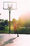 Young boy on basketball court, holding basketball, mid layup, rear view