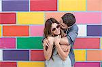Couple in front of colourful tiled wall hugging, Coney island, Brooklyn, New York, USA