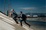 Businessmen running up riverbank, Los Angeles river, California, USA