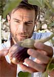 Mature man inspecting vegetables growing in garden, close-up