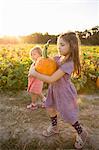 Young girl beside pumpkin patch, carrying pumpkin