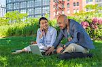 Businessman and woman sitting outdoors on grass, using laptop