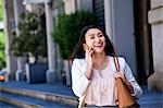 Businesswoman walking outdoors, using smartphone, smiling
