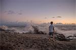Rear view of boy watching splashing waves at sunrise, Blowing Rocks Preserve, Jupiter Island, Florida, USA
