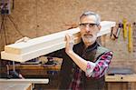 Portrait of a carpenter holding wood plank on his shoulder in a workshop