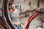 Portrait of woman fixing bicycle behind a bicycle wheel in a workshop