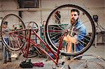Portrait of hipster crossing arms while standing behind a bicycle wheel in a workshop