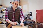 Portrait of carpenter perfecting wood plank form with a work tool in his workshop