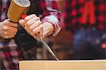 Close-up of carpenter perfecting wood plank form with a mallet in his workshop